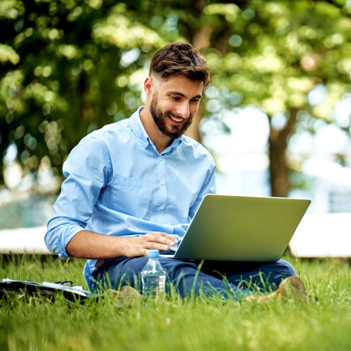 Teacher happily grading student essays on a laptop outdoors, enjoying the efficiency of AI grading tools