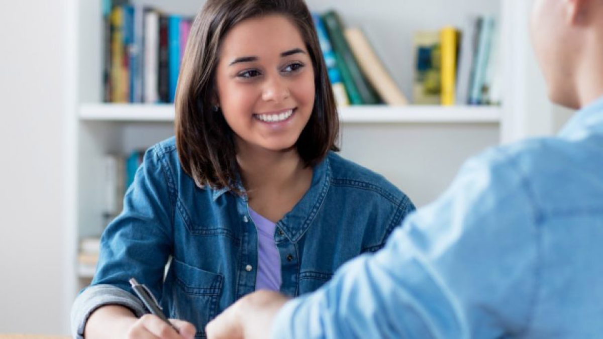 Student smiling, receiving AI essay grader feedback from her teacher